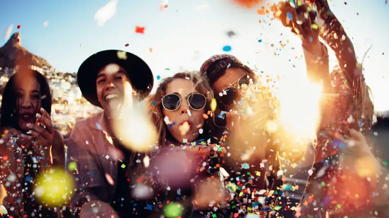 Eine Gruppe Feiernde mit Konfetti und Luftschlangen vor einem blauen Himmel Eine Gruppe Feiernde mit Konfetti und Luftschlangen vor einem blauen Himmel