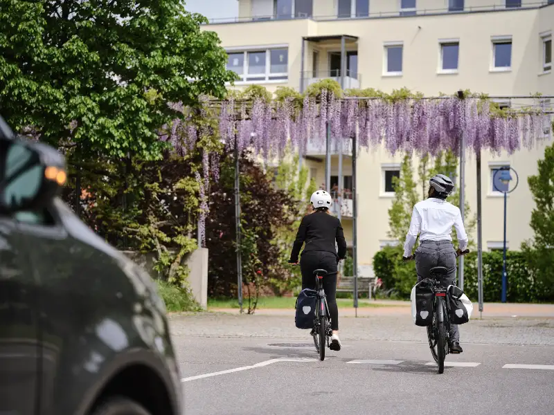 Zwei Jobradlerinnen fahren vom Betrachter weg auf ein Mietshaus zu. Zwei Jobradlerinnen fahren vom Betrachter weg auf ein Mietshaus zu.