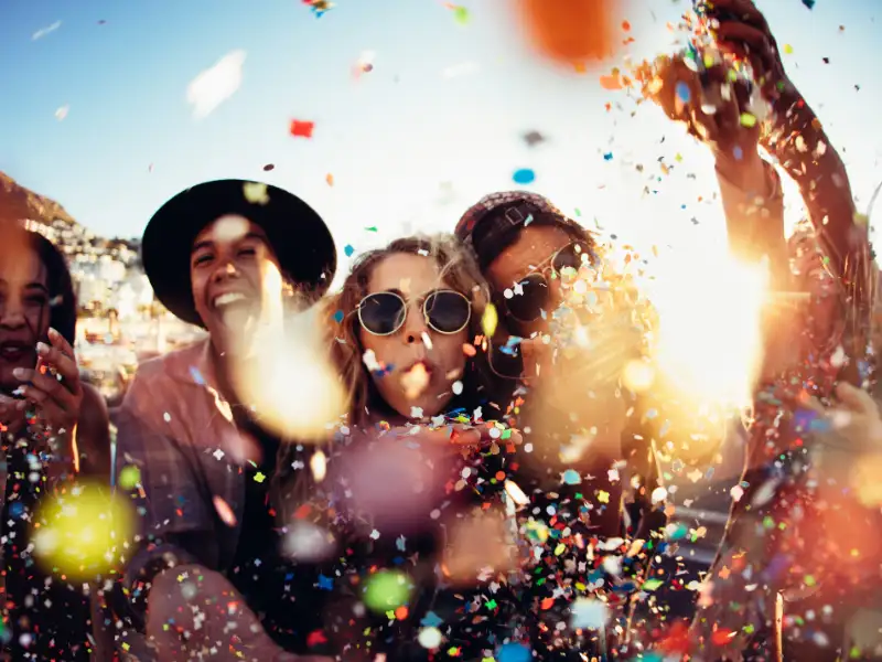 Eine Gruppe Feiernde mit Konfetti und Luftschlangen vor einem blauen Himmel Eine Gruppe Feiernde mit Konfetti und Luftschlangen vor einem blauen Himmel