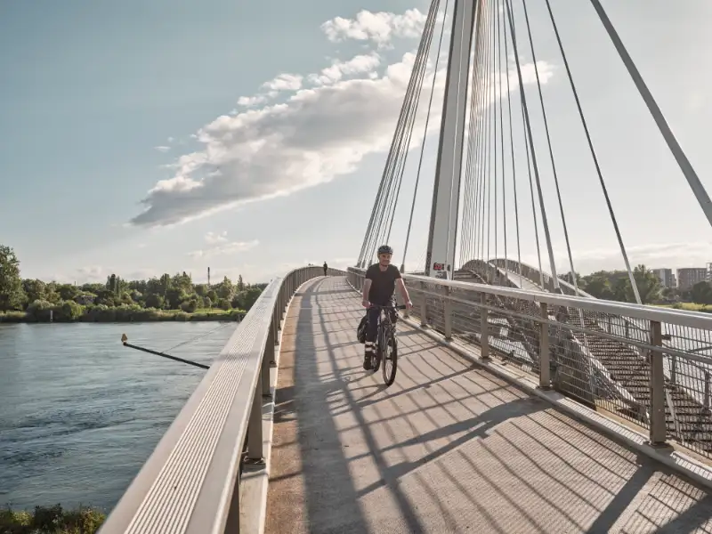 Radfahrer in Arbeitskleidung auf Fahrradbrücke über Fluss Radfahrer in Arbeitskleidung auf Fahrradbrücke über Fluss