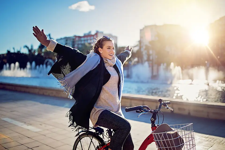 Junge Frau radelt freihändig, mit offenen Armen im Sonnenuntergang. Es ist Winter und es liegt Schnee. Junge Frau radelt freihändig, mit offenen Armen im Sonnenuntergang. Es ist Winter und es liegt Schnee.